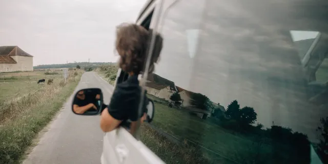 Ein Mann lehnt aus dem offenen Fenster eines Campers und blickt auf die Straße die der Camper langfährt.