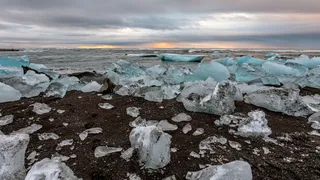 Diamond Beach as a highlight of the round trip Island: icebows lie on the beach in the dark sand, while in the background the sun goes down