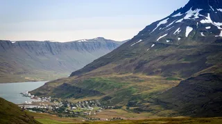 The Island Tour 10 days also passes the Ostfjorden: Here you can see a fjord next to a green mountain ridge which is partly still covered with snow