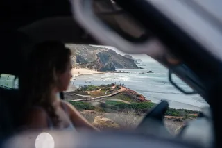 A woman drives a California Beach Van and looks out the window, you see the Portuguese Algarve coast and the sea. Caribbean in Europe is also found in Portugal.