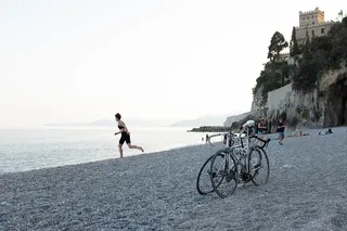 A woman in bicycle clothing runs towards the sea, on the beach standing on the beach.