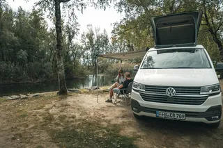 1 Personen sitzen vor CamperBoys Camper in Slowenien unter aufgestellter Markise 