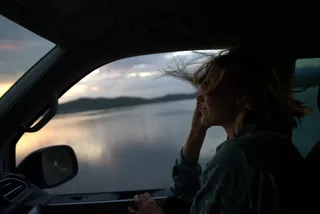 Frau mit wehenden Haaren schaut aus dem Fenster ihres Off Campers
